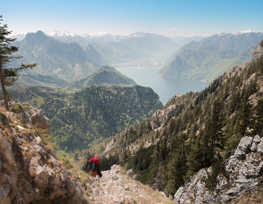 Hiker with red backpack overlooking alpine lake and snow-capped peaks